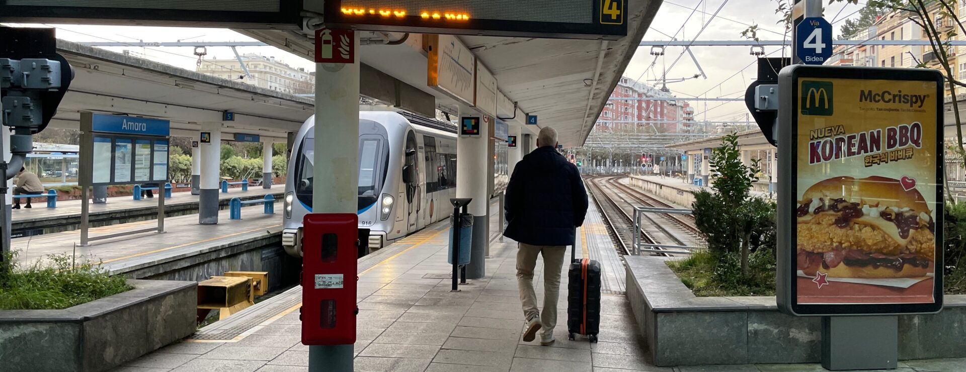 Reiziger met koffer loopt over het perron van station Amara-Donostia naar het Baskische treintje